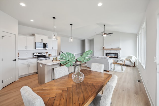 dining space with ceiling fan, a healthy amount of sunlight, a fireplace, and vaulted ceiling