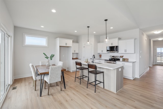 kitchen with white cabinetry, a wealth of natural light, stainless steel appliances, decorative light fixtures, and a kitchen island with sink