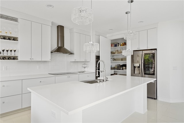 kitchen featuring decorative light fixtures, light tile floors, wall chimney range hood, white cabinets, and a kitchen island with sink