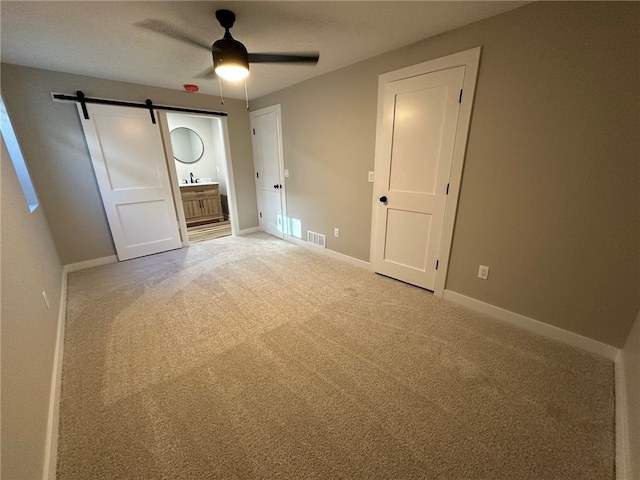 unfurnished bedroom featuring carpet flooring, a barn door, ceiling fan, and connected bathroom