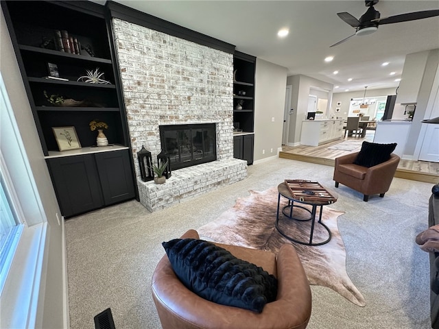 living room with ceiling fan, light colored carpet, built in features, and a brick fireplace