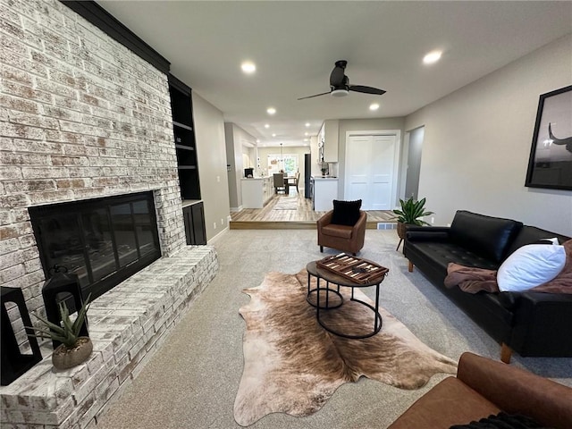 carpeted living room featuring ceiling fan, built in features, and a brick fireplace