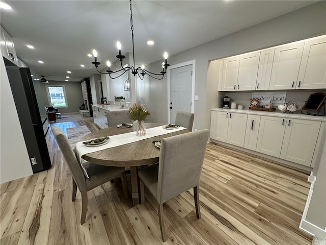 dining area with ceiling fan with notable chandelier and light hardwood / wood-style flooring