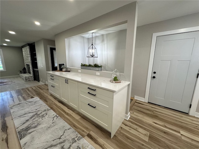 bar featuring white cabinets, light wood-type flooring, a fireplace, and hanging light fixtures