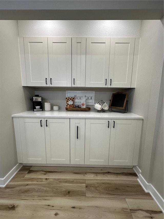 bar with white cabinetry and light wood-type flooring