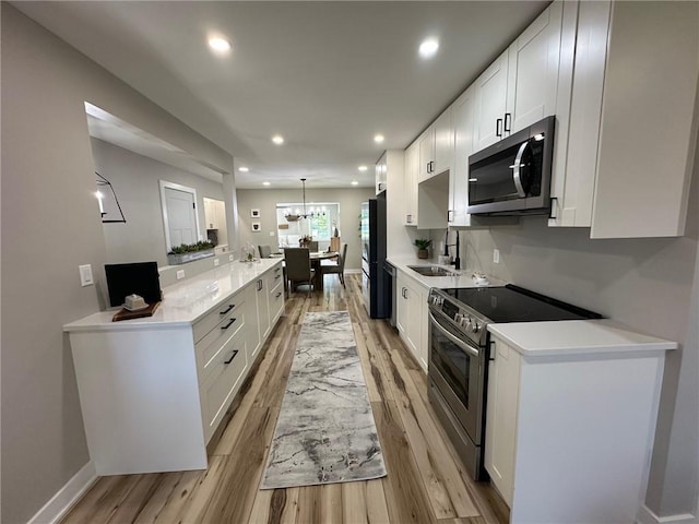 kitchen featuring sink, stainless steel appliances, light hardwood / wood-style floors, decorative light fixtures, and white cabinets