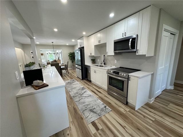 kitchen with white cabinetry, hanging light fixtures, appliances with stainless steel finishes, and light hardwood / wood-style flooring