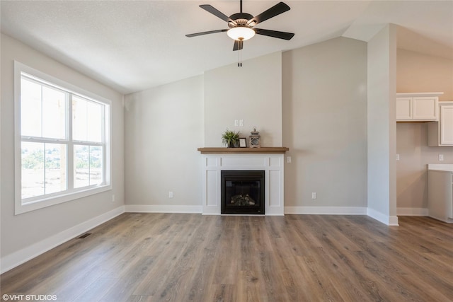 unfurnished living room with baseboards, a glass covered fireplace, ceiling fan, vaulted ceiling, and light wood-type flooring