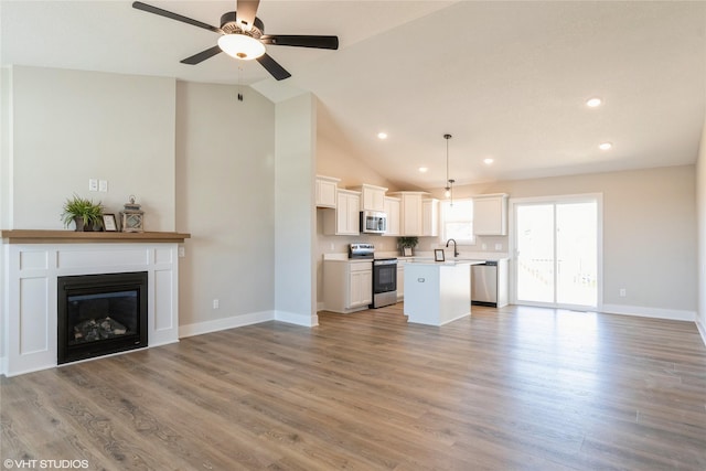 kitchen featuring open floor plan, stainless steel appliances, light wood finished floors, and a kitchen island with sink