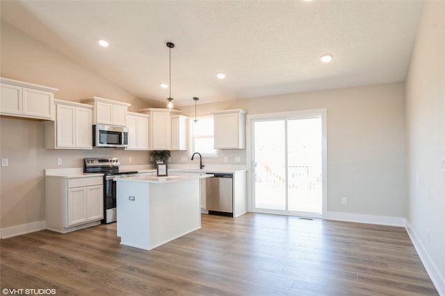 kitchen with vaulted ceiling, stainless steel appliances, a kitchen island, and white cabinetry