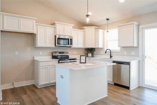 kitchen with appliances with stainless steel finishes, a center island, vaulted ceiling, light countertops, and white cabinetry