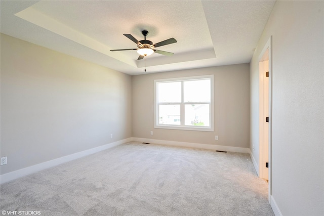 unfurnished room with light carpet, baseboards, ceiling fan, a tray ceiling, and a textured ceiling