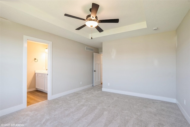 unfurnished bedroom featuring light carpet, visible vents, a tray ceiling, and baseboards