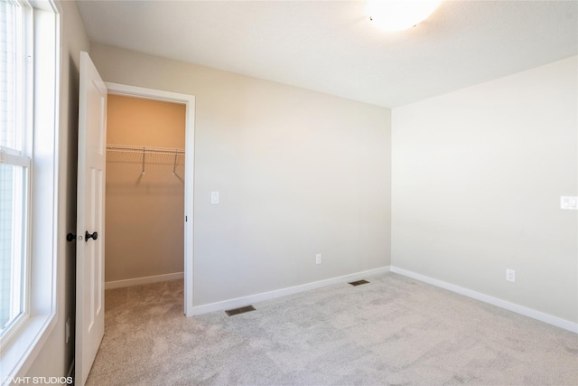 unfurnished bedroom with carpet flooring, a walk in closet, and visible vents