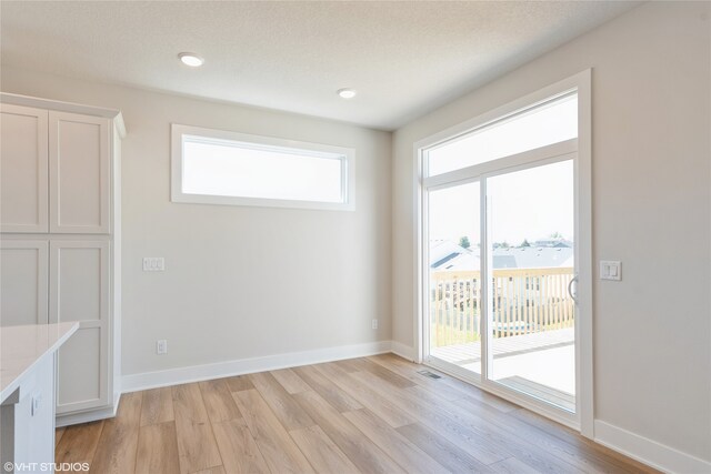 unfurnished dining area featuring a textured ceiling and light hardwood / wood-style floors