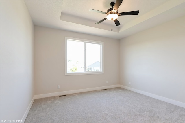 carpeted spare room with ceiling fan and a raised ceiling