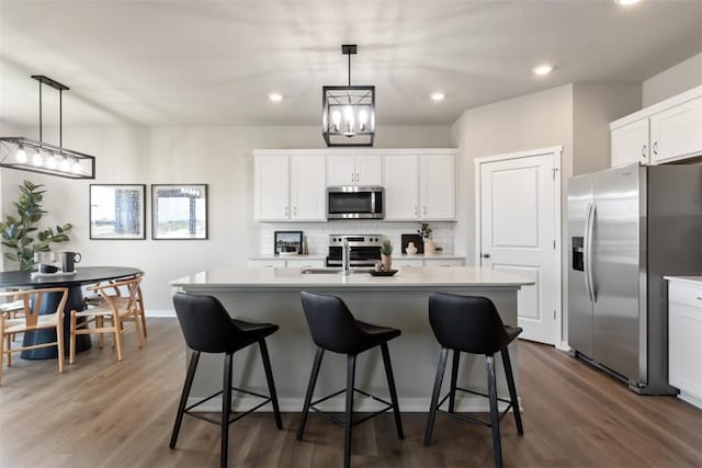 kitchen with white cabinets, an island with sink, decorative light fixtures, dark hardwood / wood-style flooring, and stainless steel appliances