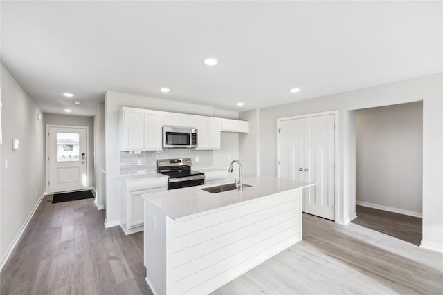 kitchen with appliances with stainless steel finishes, white cabinetry, sink, and a center island with sink