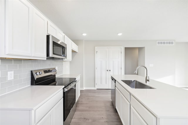 kitchen featuring appliances with stainless steel finishes, sink, light wood-type flooring, white cabinets, and a center island with sink