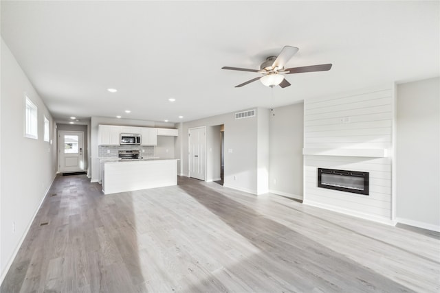 unfurnished living room featuring a large fireplace, light wood-type flooring, and ceiling fan