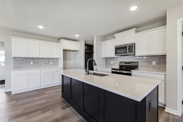 kitchen with hardwood / wood-style flooring, a center island with sink, white cabinetry, and appliances with stainless steel finishes