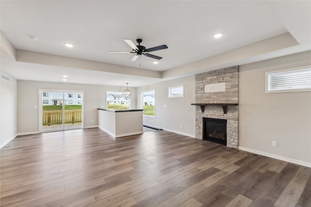 unfurnished living room with ceiling fan with notable chandelier, a stone fireplace, dark hardwood / wood-style flooring, and a wealth of natural light