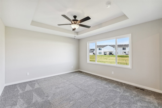 carpeted empty room featuring ceiling fan and a raised ceiling