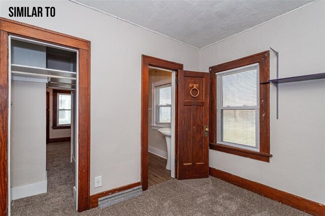 unfurnished bedroom featuring a textured ceiling, a closet, multiple windows, and dark carpet