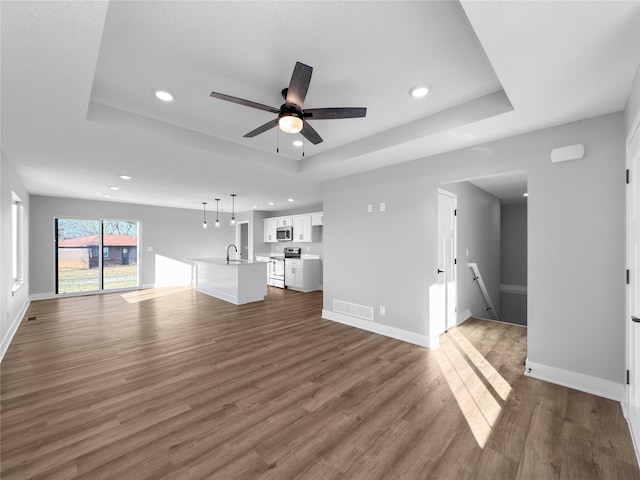 unfurnished living room featuring ceiling fan, dark hardwood / wood-style flooring, sink, and a tray ceiling