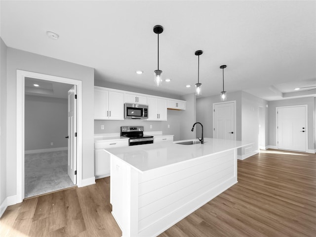 kitchen with white cabinetry, sink, hanging light fixtures, stainless steel appliances, and an island with sink