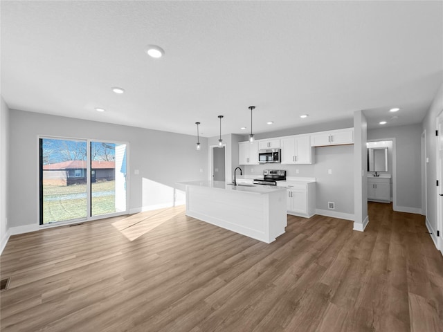 kitchen with appliances with stainless steel finishes, decorative light fixtures, hardwood / wood-style flooring, white cabinets, and an island with sink