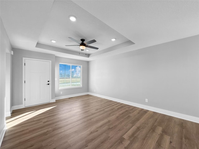 empty room with a tray ceiling, ceiling fan, dark hardwood / wood-style flooring, and a textured ceiling