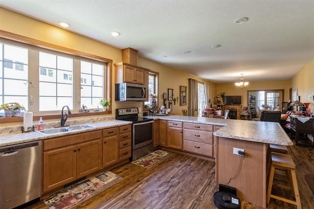 kitchen with dark wood-style floors, a peninsula, a sink, appliances with stainless steel finishes, and a kitchen bar