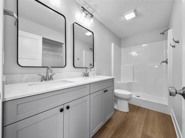 bathroom with hardwood / wood-style floors, vanity, a shower, toilet, and a textured ceiling