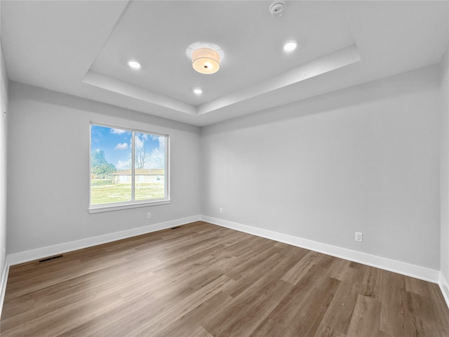 unfurnished room with wood-type flooring and a tray ceiling