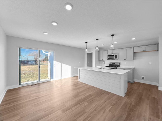 kitchen with gray cabinetry, hanging light fixtures, stainless steel appliances, light hardwood / wood-style flooring, and an island with sink