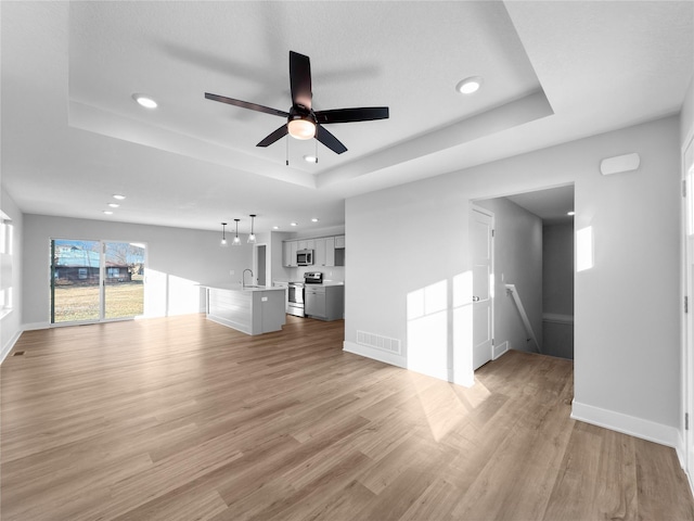 unfurnished living room featuring a raised ceiling, light hardwood / wood-style flooring, ceiling fan, and sink