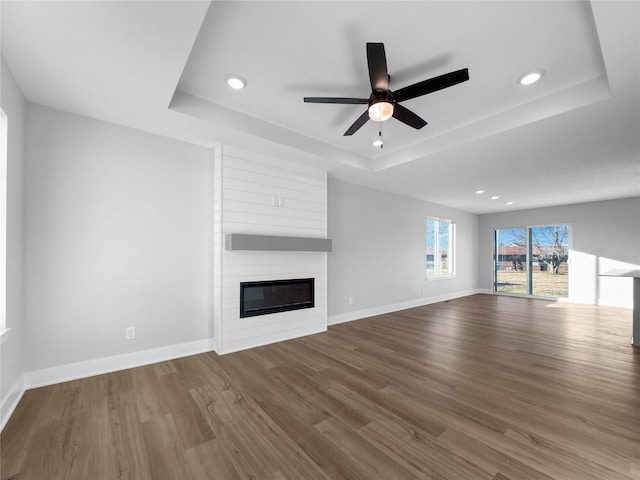 unfurnished living room with hardwood / wood-style flooring, ceiling fan, a raised ceiling, and a fireplace