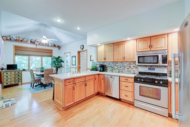 kitchen with lofted ceiling, sink, light hardwood / wood-style flooring, stainless steel appliances, and kitchen peninsula