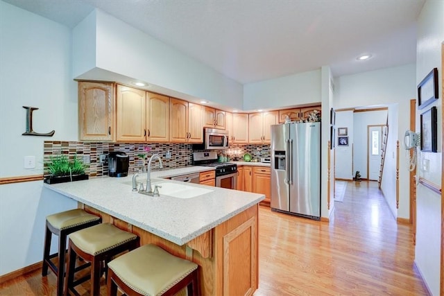 kitchen featuring appliances with stainless steel finishes, sink, backsplash, light hardwood / wood-style floors, and kitchen peninsula