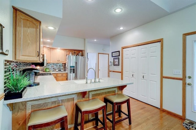 kitchen with sink, stainless steel appliances, light hardwood / wood-style floors, a kitchen bar, and kitchen peninsula