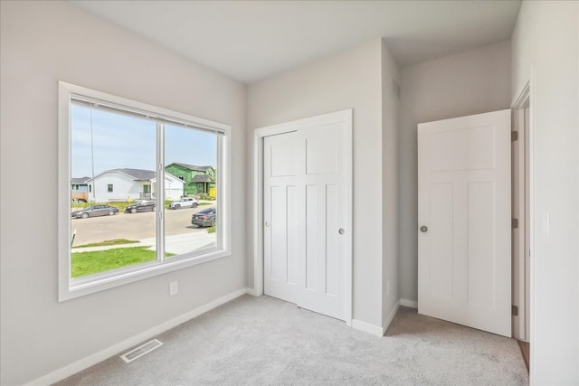 unfurnished bedroom with light carpet, a residential view, visible vents, and baseboards