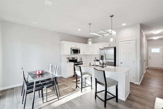 kitchen featuring light hardwood / wood-style floors, an island with sink, white cabinets, stainless steel appliances, and decorative light fixtures