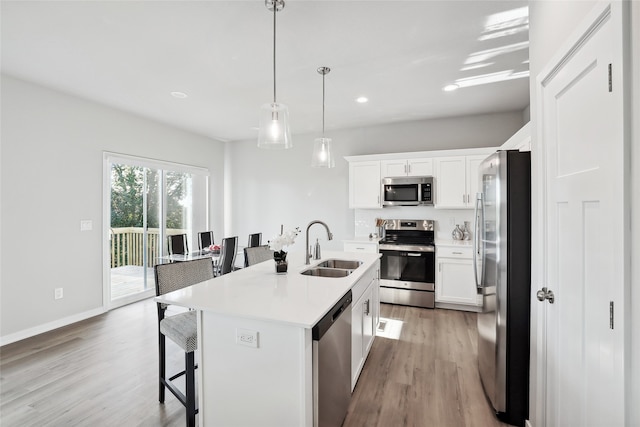 kitchen featuring white cabinets, a center island with sink, stainless steel appliances, and a sink