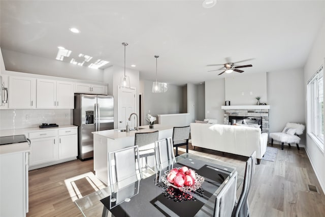 kitchen featuring a kitchen island with sink, stainless steel appliances, white cabinetry, and pendant lighting