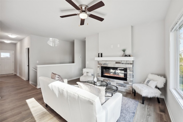 living area with visible vents, baseboards, a ceiling fan, wood finished floors, and a stone fireplace