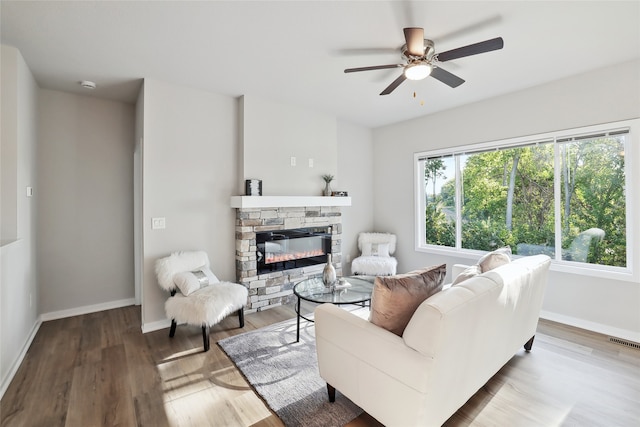 living area featuring ceiling fan, a stone fireplace, wood finished floors, visible vents, and baseboards