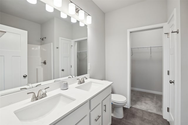 bathroom featuring toilet, double vanity, a sink, and a walk in closet