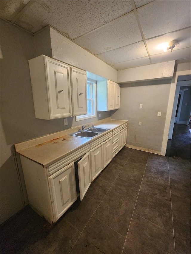 kitchen featuring white cabinets, a drop ceiling, dark tile patterned floors, and sink