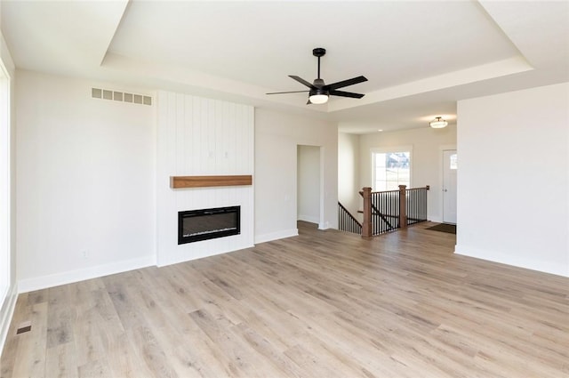 unfurnished living room with a tray ceiling, ceiling fan, a fireplace, and light hardwood / wood-style floors